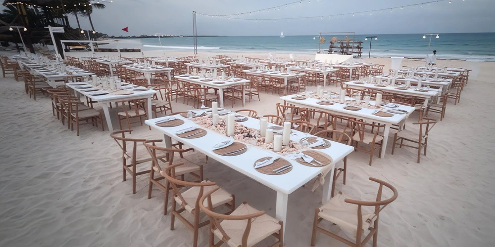 Central Beach Venue at Secrets Maroma Beach featuring an elegant beachfront reception setup with long white tables, wooden chairs, candle centerpieces, and Caribbean Sea views.