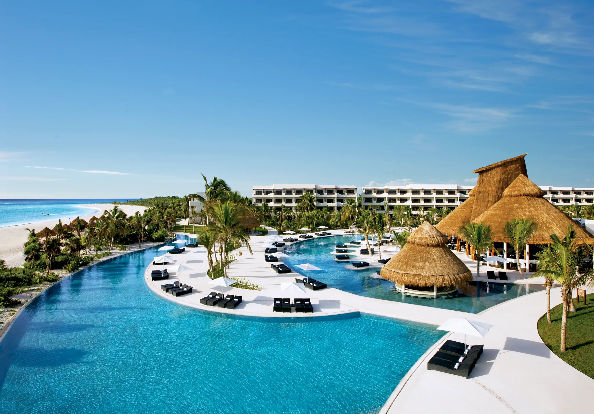 Expansive infinity pools and thatched-roof palapas at Secrets Maroma Beach Riviera Cancun overlooking the Caribbean Sea.