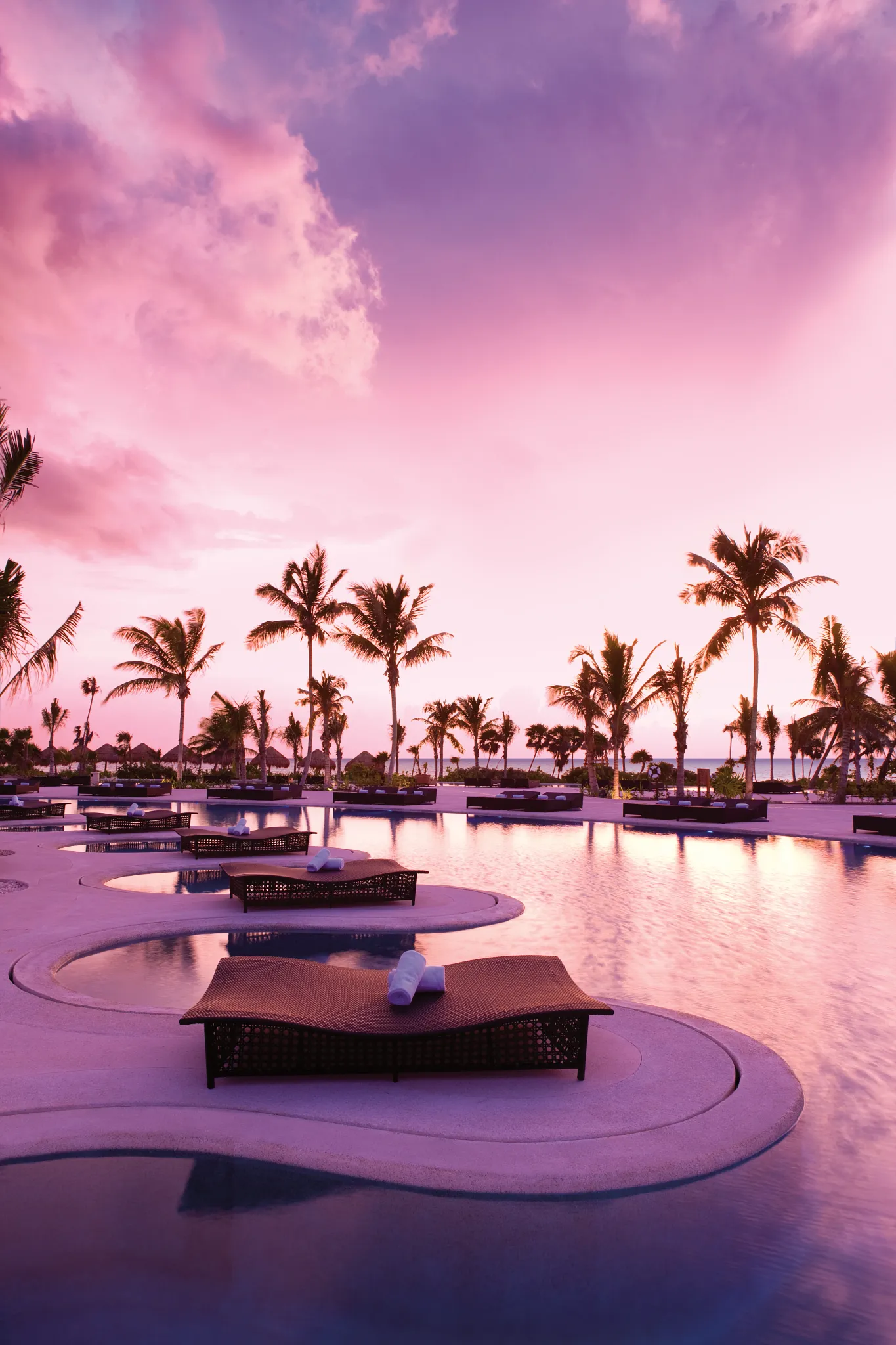 Sunrise over the infinity pool and palm trees at Secrets Maroma Beach Riviera Cancun on Maroma Beach.